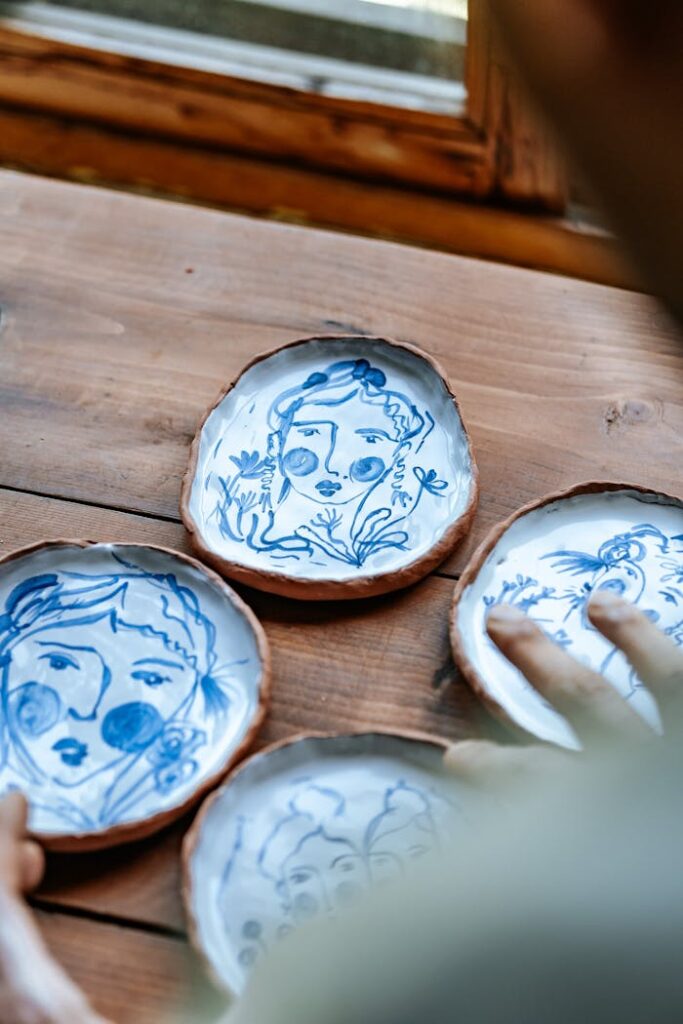 Rustic ceramic plates featuring blue painted artistic face designs on a wooden table.