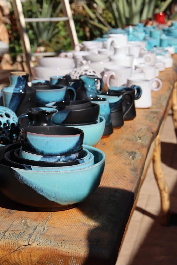 A variety of blue and white ceramic bowls and mugs displayed on a wooden table outdoors.
